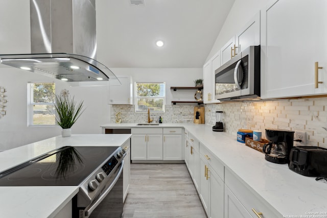 kitchen featuring lofted ceiling, white cabinets, sink, appliances with stainless steel finishes, and island range hood