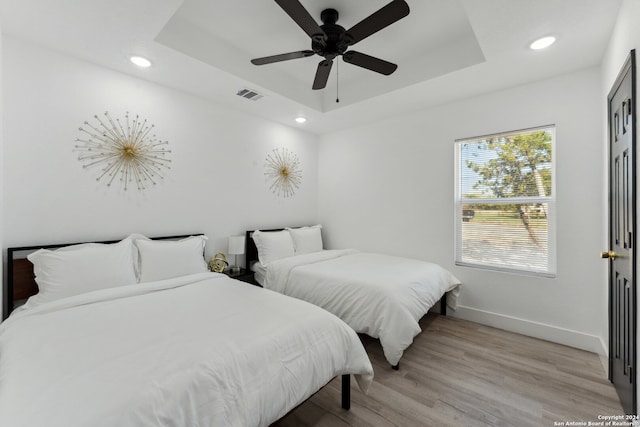 bedroom with a tray ceiling, ceiling fan, and light hardwood / wood-style floors