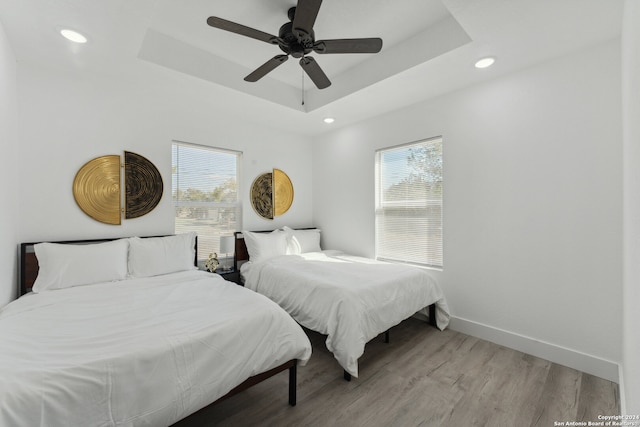 bedroom with ceiling fan, light wood-type flooring, and a tray ceiling