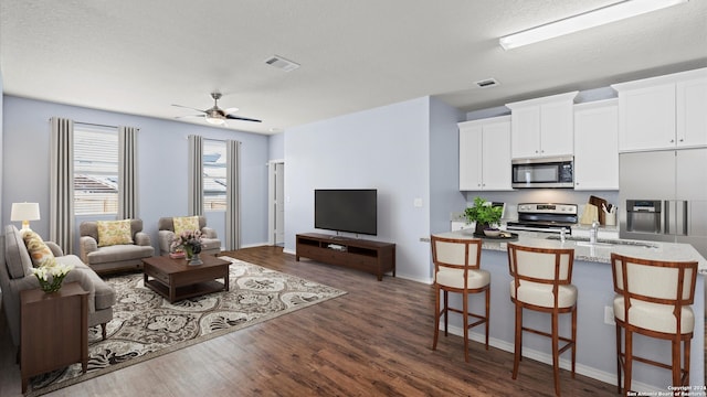 living room featuring a textured ceiling, ceiling fan, dark wood-type flooring, and sink