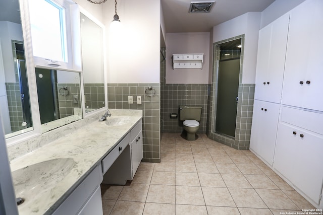 bathroom with tile patterned floors, vanity, a shower with door, tile walls, and toilet