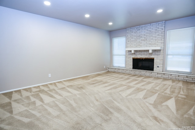 unfurnished living room featuring light carpet, a fireplace, and a healthy amount of sunlight