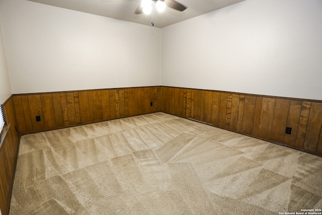 carpeted empty room featuring ceiling fan and wooden walls