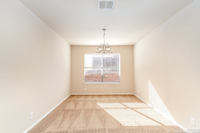 spare room with a notable chandelier and light colored carpet