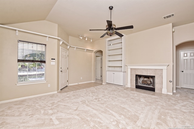 unfurnished living room with lofted ceiling, a tile fireplace, ceiling fan, built in features, and light colored carpet