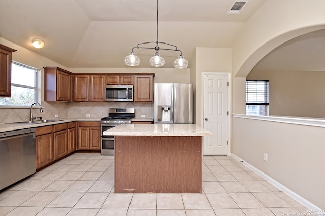 kitchen featuring hanging light fixtures, vaulted ceiling, light stone countertops, a kitchen island, and stainless steel appliances