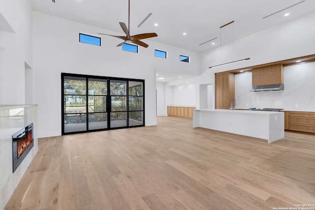 unfurnished living room with ceiling fan, sink, a high ceiling, and light hardwood / wood-style flooring