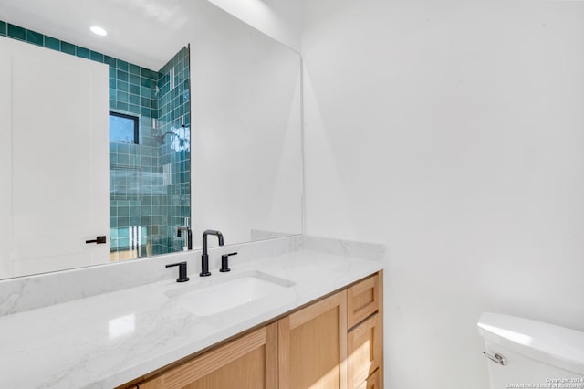 bathroom featuring a tile shower, vanity, and toilet