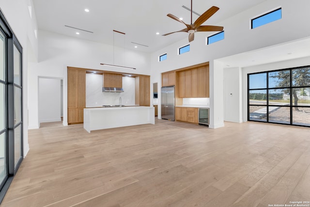 unfurnished living room with ceiling fan, wine cooler, light wood-type flooring, and a high ceiling