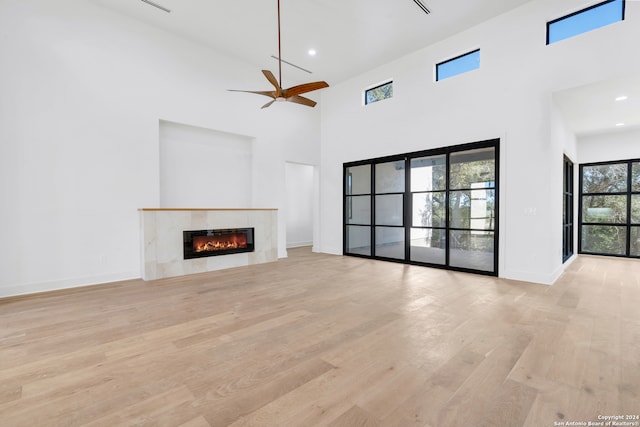 unfurnished living room with a high end fireplace, a high ceiling, light hardwood / wood-style floors, and ceiling fan