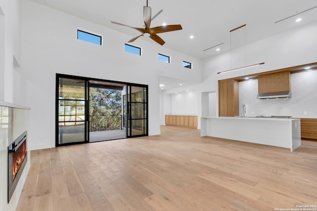 unfurnished living room featuring ceiling fan, light wood-type flooring, sink, and a high ceiling