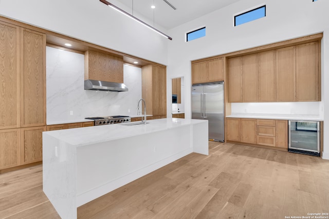 kitchen featuring a high ceiling, sink, wine cooler, light wood-type flooring, and appliances with stainless steel finishes