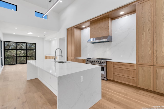 kitchen featuring a towering ceiling, wall chimney exhaust hood, high end stove, sink, and light hardwood / wood-style floors