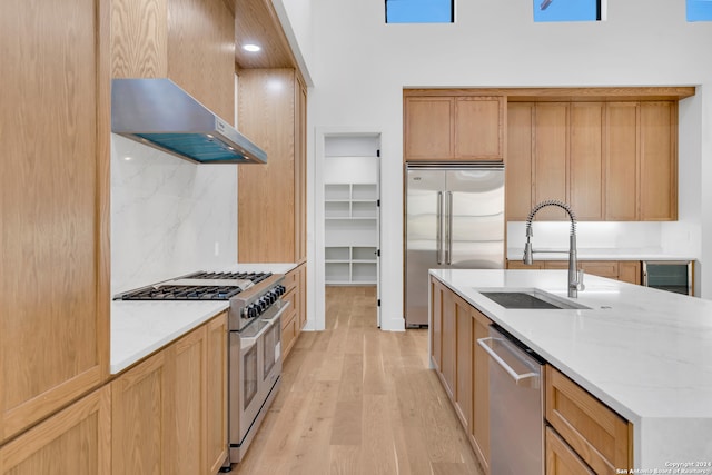 kitchen featuring wall chimney exhaust hood, premium appliances, a kitchen island with sink, sink, and light hardwood / wood-style flooring