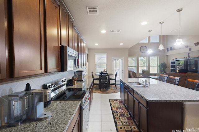 kitchen with appliances with stainless steel finishes, tasteful backsplash, light stone counters, sink, and a center island with sink