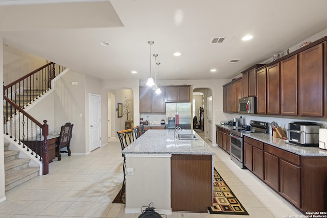 kitchen featuring sink, stainless steel appliances, light stone counters, an island with sink, and decorative light fixtures