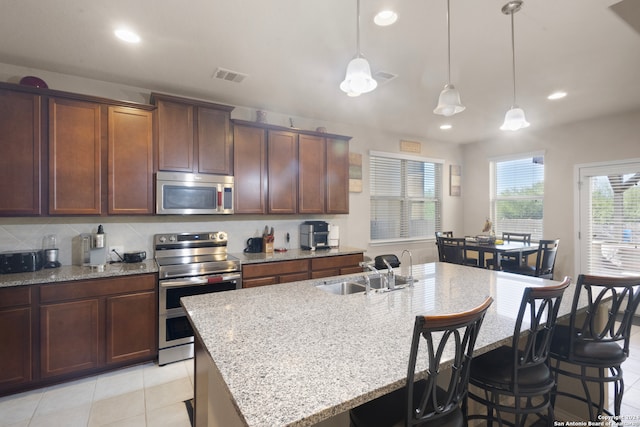 kitchen featuring pendant lighting, sink, stainless steel appliances, and an island with sink