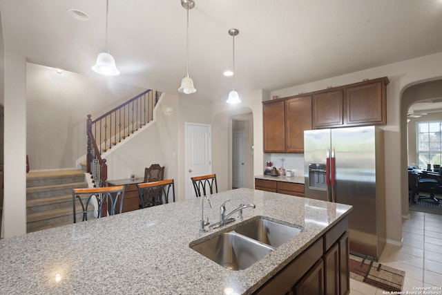 kitchen featuring stainless steel fridge, sink, light stone countertops, and decorative light fixtures