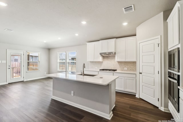 kitchen featuring visible vents, under cabinet range hood, decorative backsplash, appliances with stainless steel finishes, and dark wood-style flooring