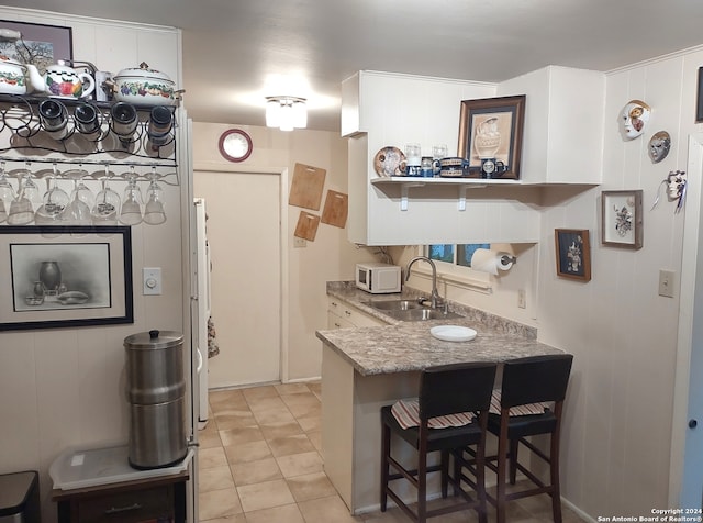 kitchen featuring a breakfast bar area, light tile patterned floors, open shelves, white microwave, and a sink