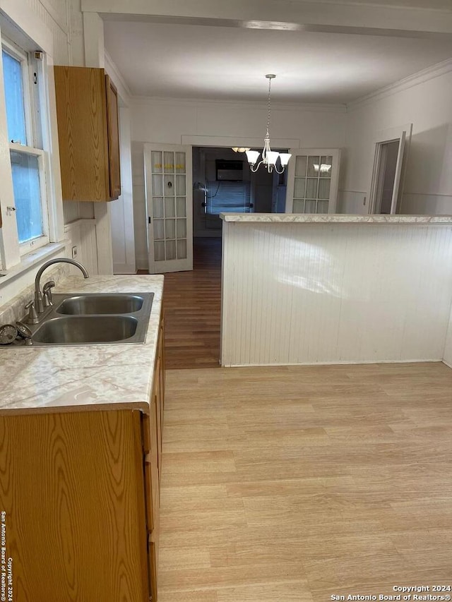 kitchen featuring sink, hanging light fixtures, a notable chandelier, crown molding, and light wood-type flooring