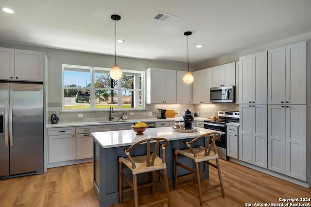 kitchen featuring appliances with stainless steel finishes, a center island, decorative light fixtures, and light hardwood / wood-style flooring