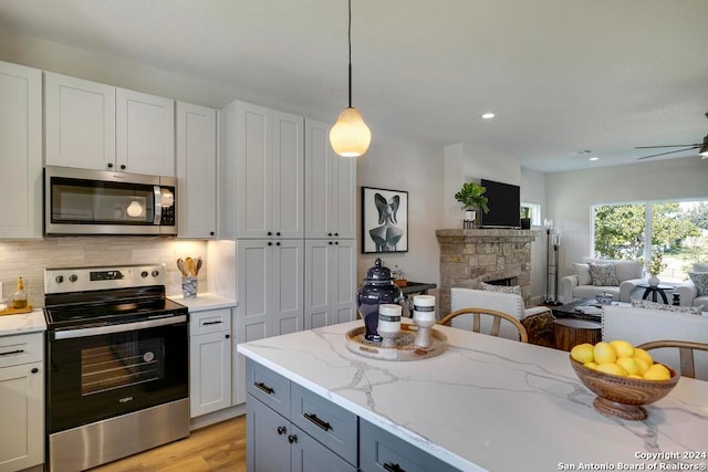 kitchen featuring white cabinetry, light stone countertops, light hardwood / wood-style flooring, a fireplace, and appliances with stainless steel finishes