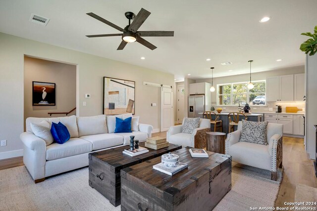 living room featuring a barn door, ceiling fan, and light hardwood / wood-style flooring