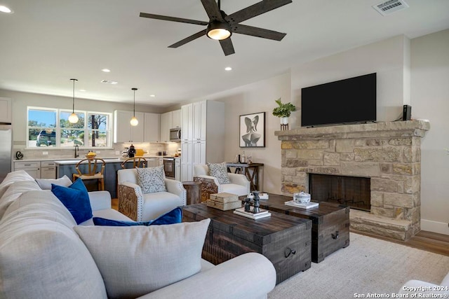 living room featuring ceiling fan, a fireplace, and light wood-type flooring