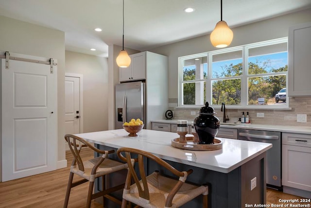 kitchen with a center island, decorative backsplash, a barn door, decorative light fixtures, and stainless steel appliances