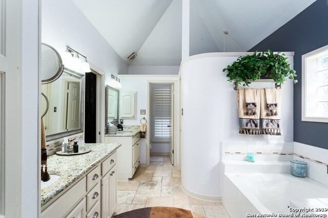 bathroom with vanity, a relaxing tiled tub, and vaulted ceiling