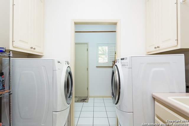 clothes washing area with washer and clothes dryer, light tile patterned flooring, and cabinets