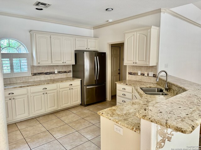 kitchen featuring white cabinets, decorative backsplash, stainless steel refrigerator, and sink