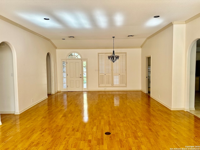 foyer entrance featuring wood-type flooring, ornamental molding, and an inviting chandelier