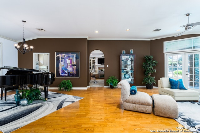 living room with french doors, hardwood / wood-style floors, lofted ceiling, ceiling fan with notable chandelier, and ornamental molding