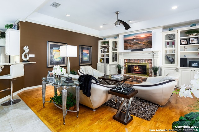 living room with ceiling fan, light hardwood / wood-style flooring, and a brick fireplace