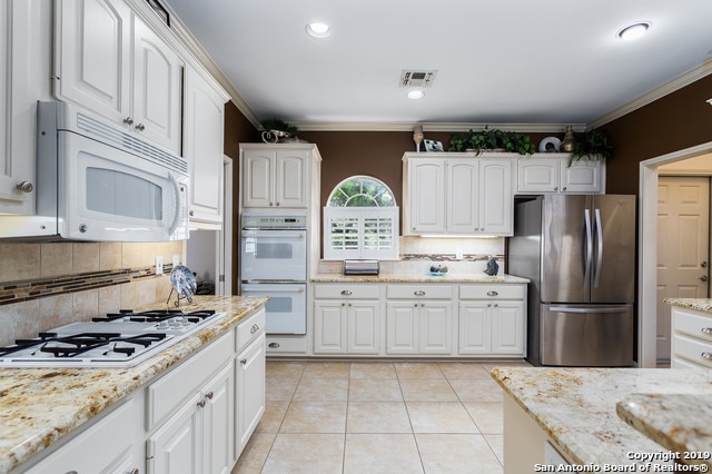 kitchen featuring decorative backsplash, white cabinets, white appliances, and ornamental molding