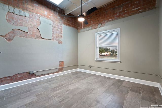 unfurnished room featuring beam ceiling, ceiling fan, and brick wall