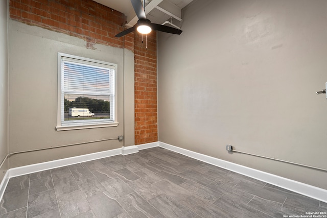 empty room with beam ceiling, ceiling fan, and brick wall