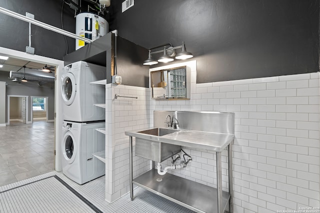 laundry area with tile patterned flooring, stacked washing maching and dryer, tile walls, and sink