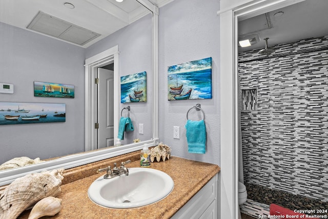 bathroom featuring vanity, toilet, ornamental molding, and tiled shower