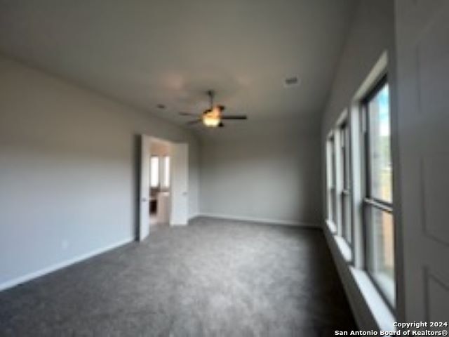 empty room featuring dark carpet, a ceiling fan, and baseboards