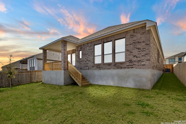 back of house featuring a yard, stairs, fence, and brick siding