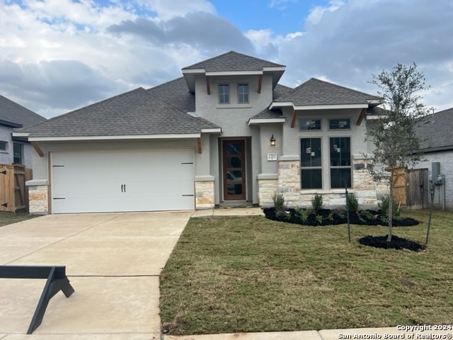 prairie-style home featuring a garage, fence, stone siding, concrete driveway, and a front lawn