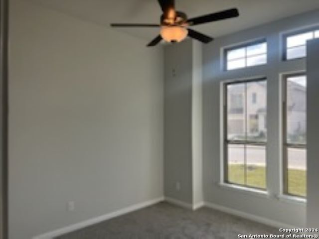 spare room with baseboards, dark carpet, and a ceiling fan