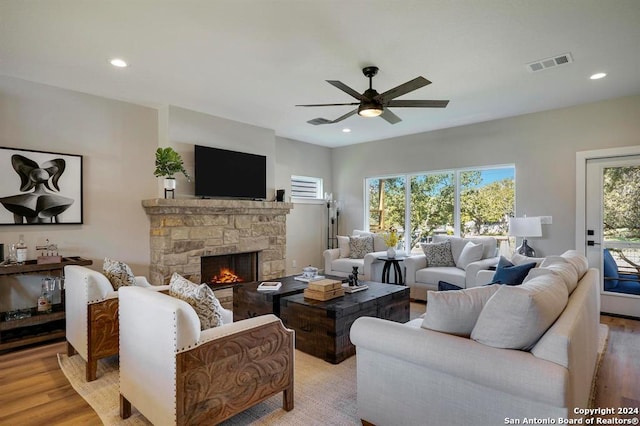 living room featuring a stone fireplace, a wealth of natural light, ceiling fan, and light wood-type flooring