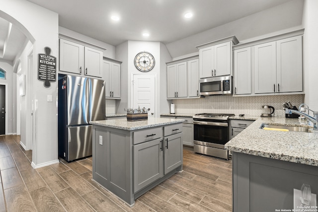 kitchen with sink, dark hardwood / wood-style floors, appliances with stainless steel finishes, a kitchen island, and light stone counters