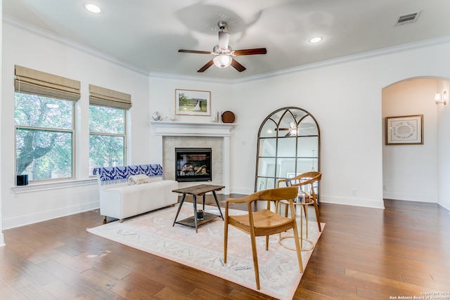 living room featuring ceiling fan, dark hardwood / wood-style flooring, ornamental molding, and a tile fireplace