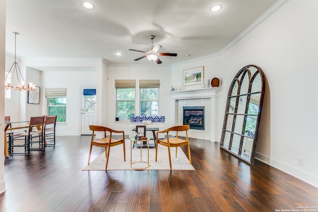 dining space featuring ornamental molding, ceiling fan with notable chandelier, dark wood-type flooring, and a tiled fireplace