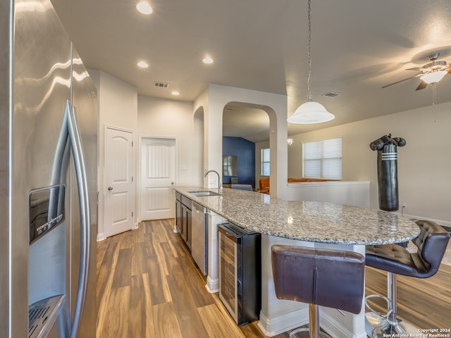 kitchen with sink, stainless steel refrigerator with ice dispenser, hanging light fixtures, light stone countertops, and beverage cooler